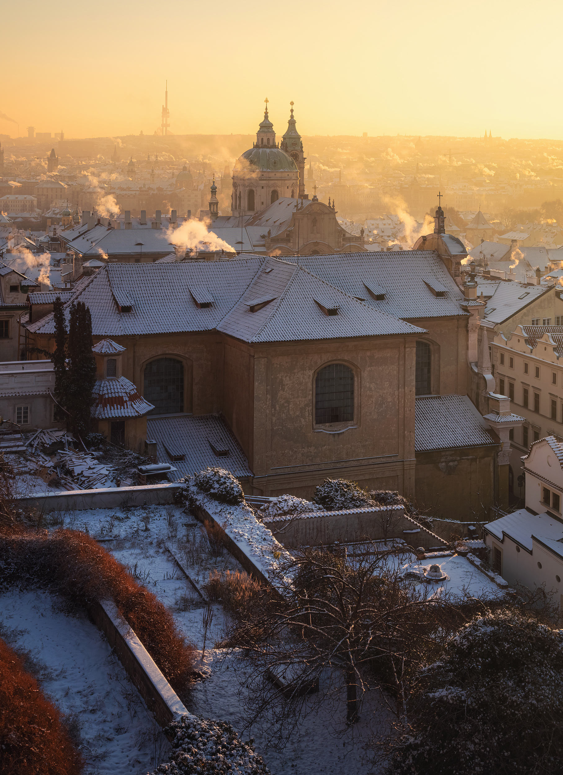 St Nicholas Church rising above winter rooftops in golden morning light, Prague