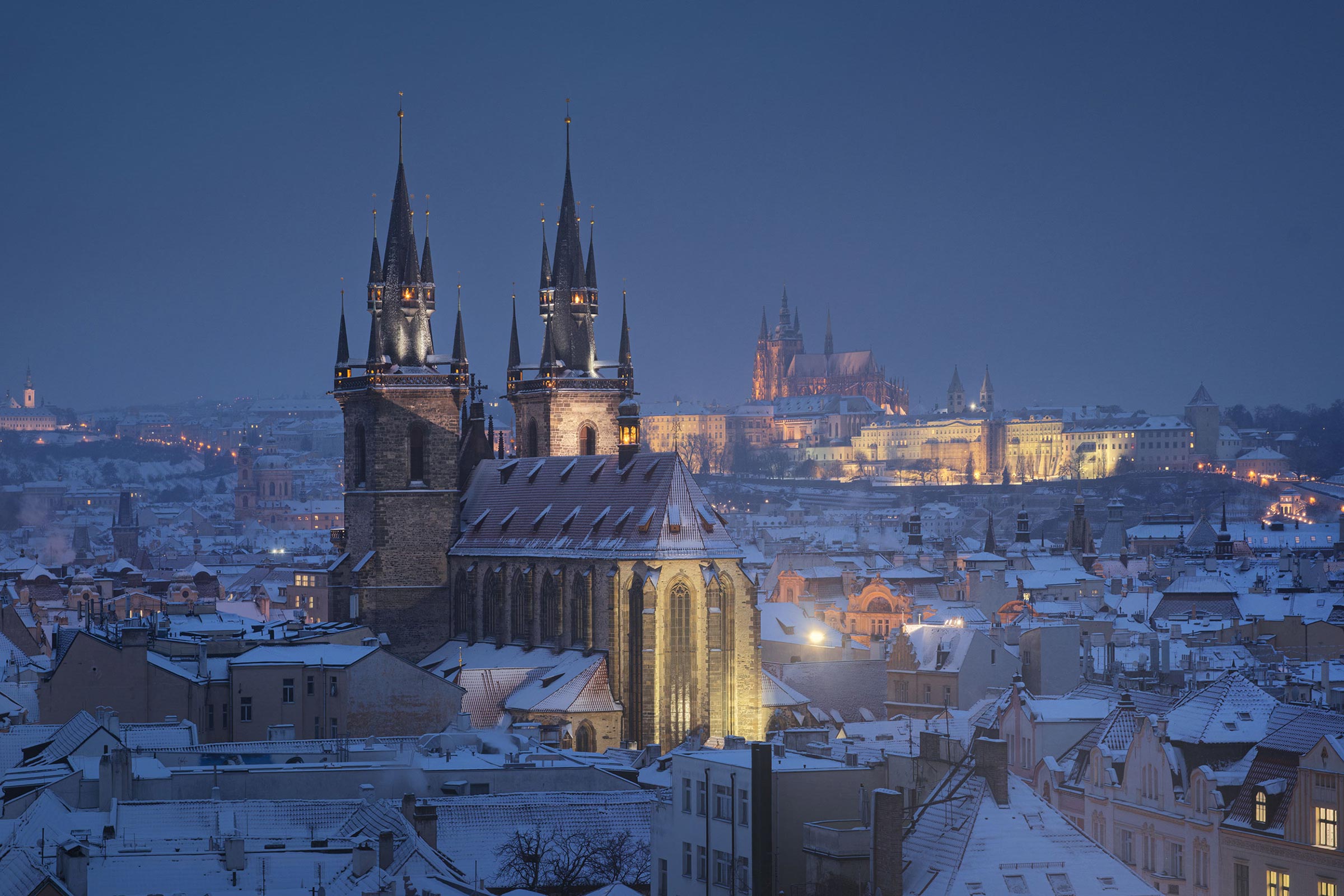 Church of Our Lady before Týn and snow-covered rooftops of Prague Old Town at blue hour, Prague Castle in the distance